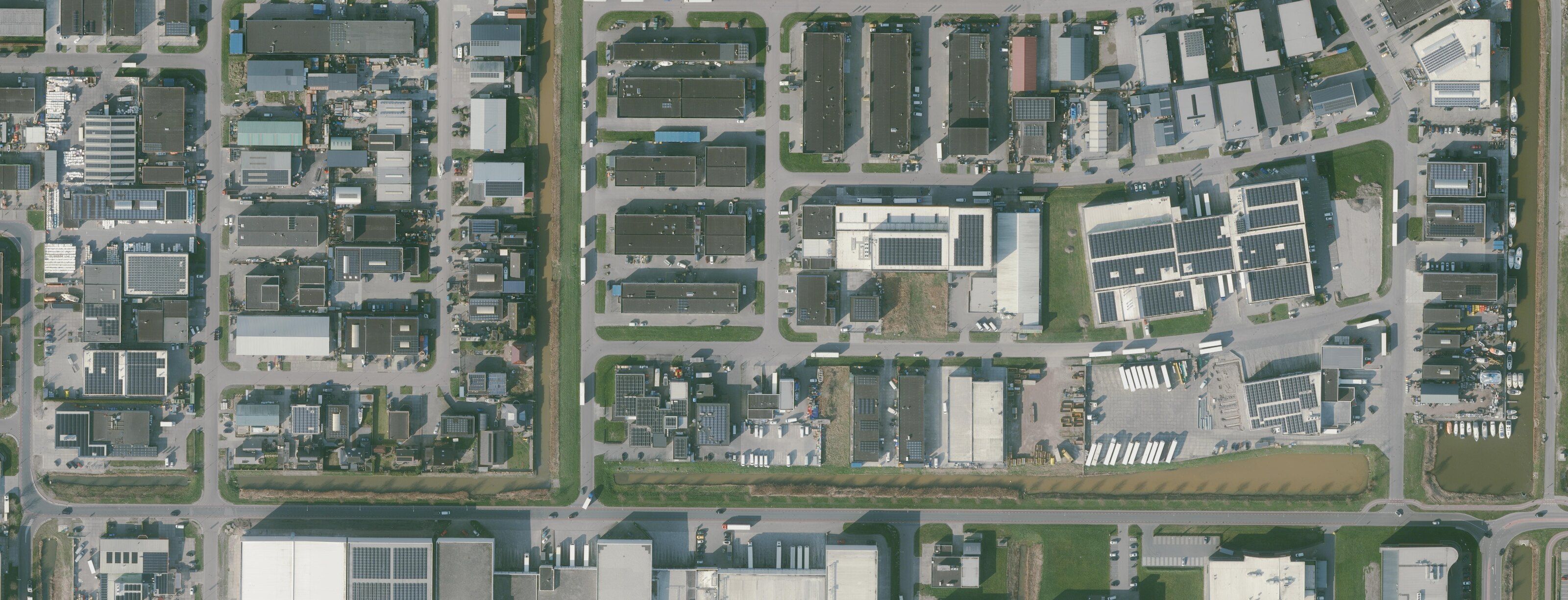 Luchtfoto recht van boven van het bedrijventerrein op Urk: rijen bedrijfshallen, daken met zonnepanelen, laadterreinen en een haventje