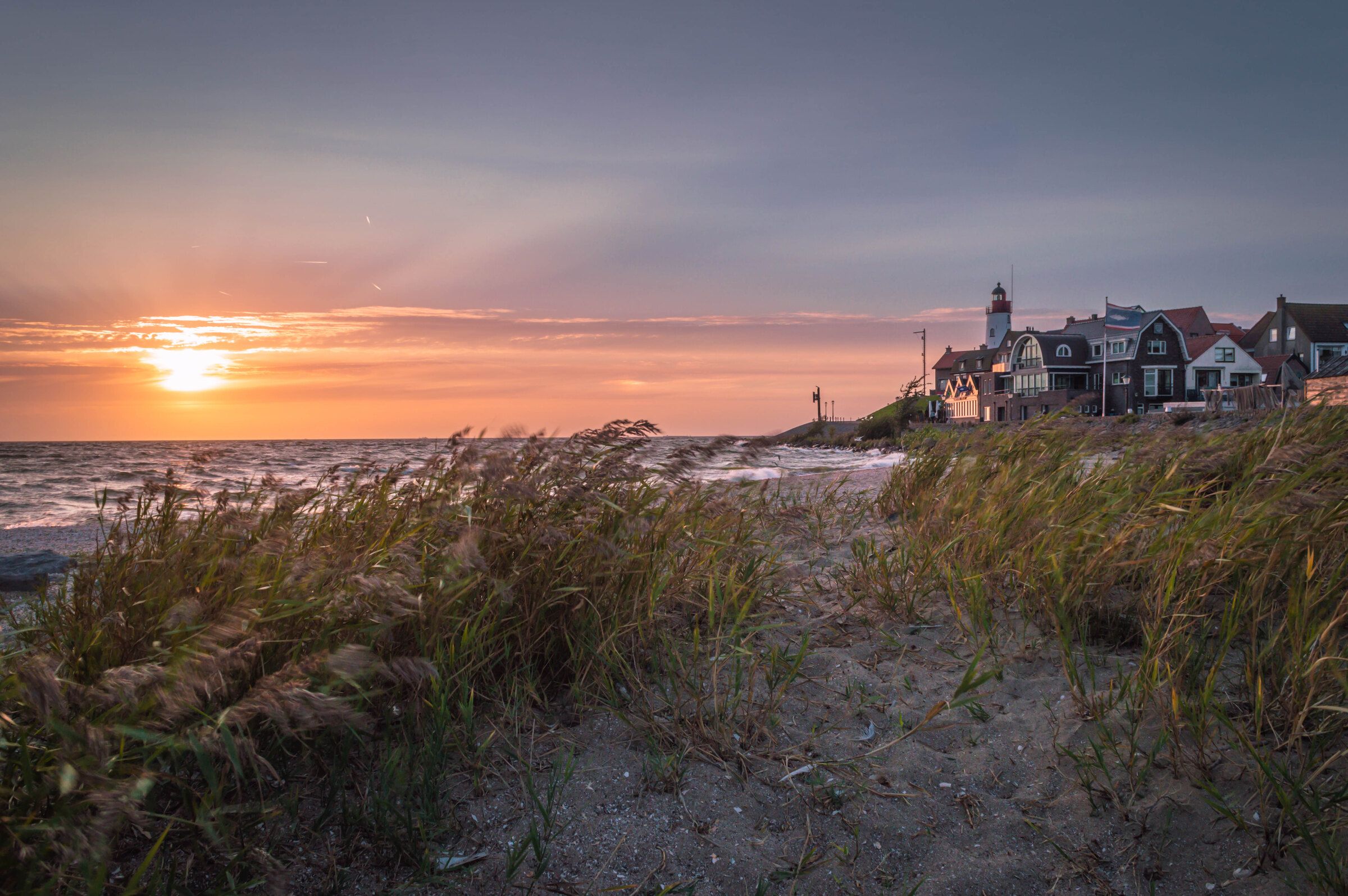 Zonsondergang boven het IJsselmeer, met riet op de voorgrond en Urk met de vuurtoren aan de horizon